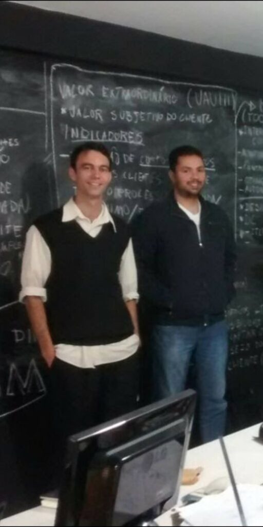 Dois integrantes da equipe da Ímpeto em frente a um quadro negro, na salinha dos primeiros anos