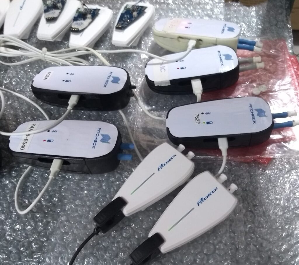 Várias unidades do Fitcheck sobre plástico-bolha: as antigas, escuras e arredondadas, e as novas, brancas