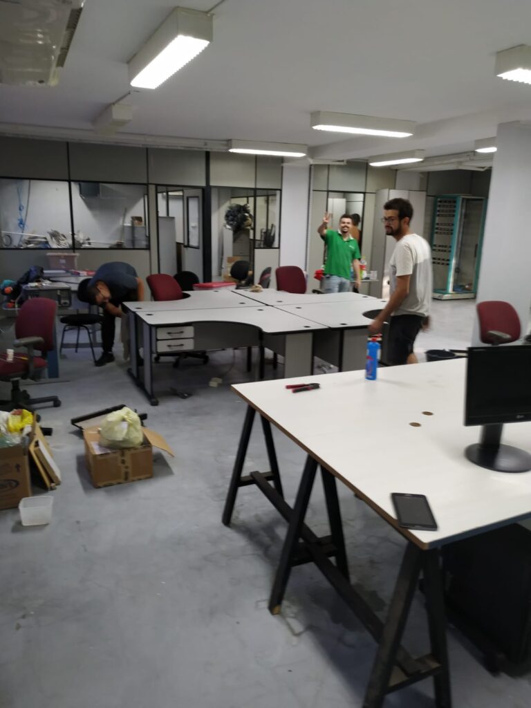 Escritório amplo ainda em arrumação, com mesas e cadeiras sendo posicionadas