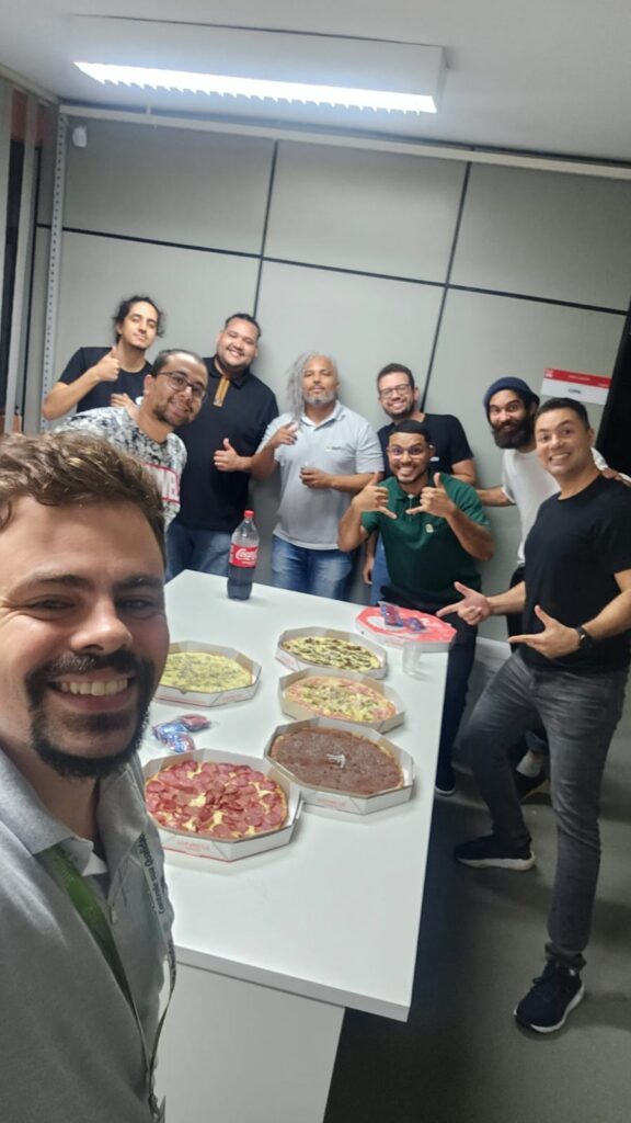 Selfie da equipe ao redor de uma mesa com várias pizzas