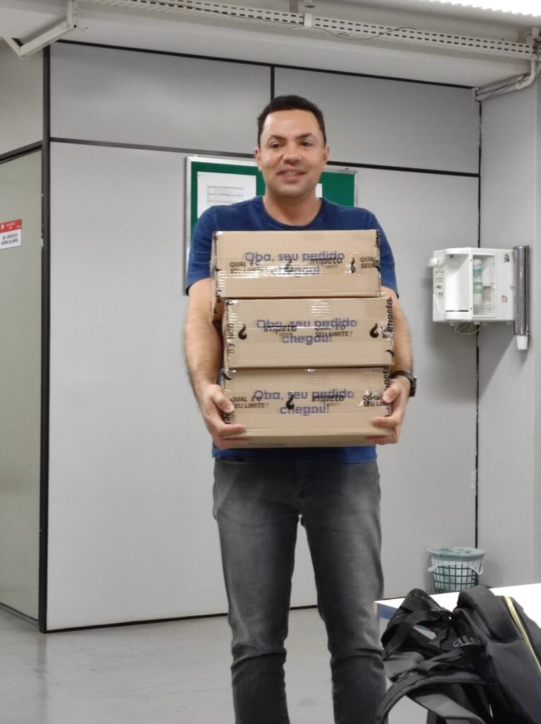 Rafael sorrindo e segurando três caixas da Ímpeto empilhadas